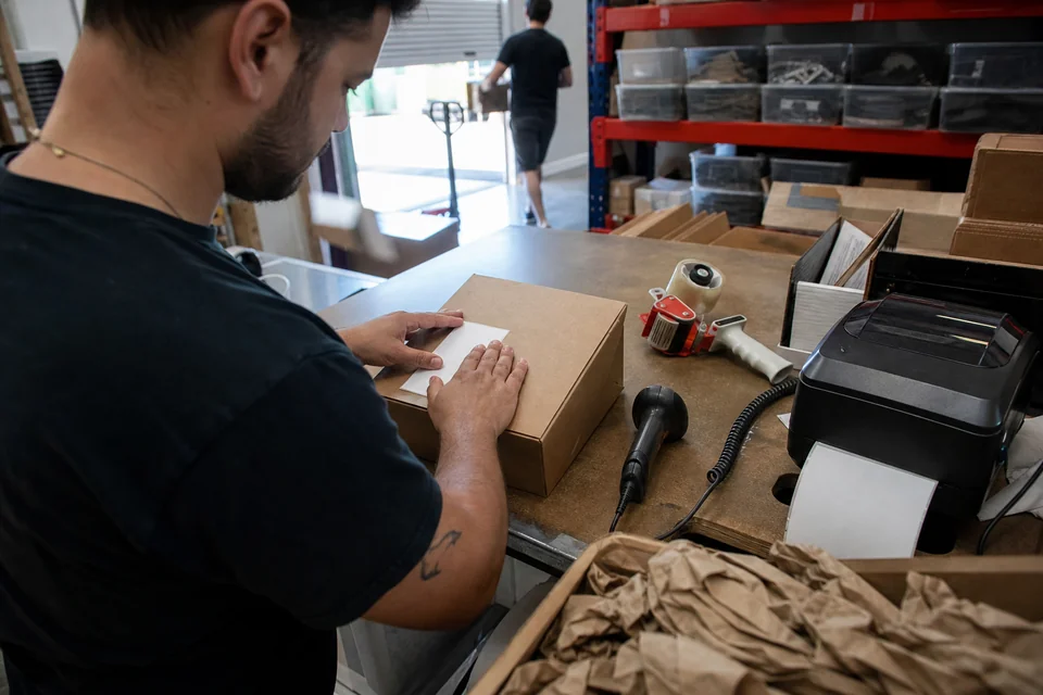 Packer pressing a freshly printed shipping label onto a box at a warehouse packing station